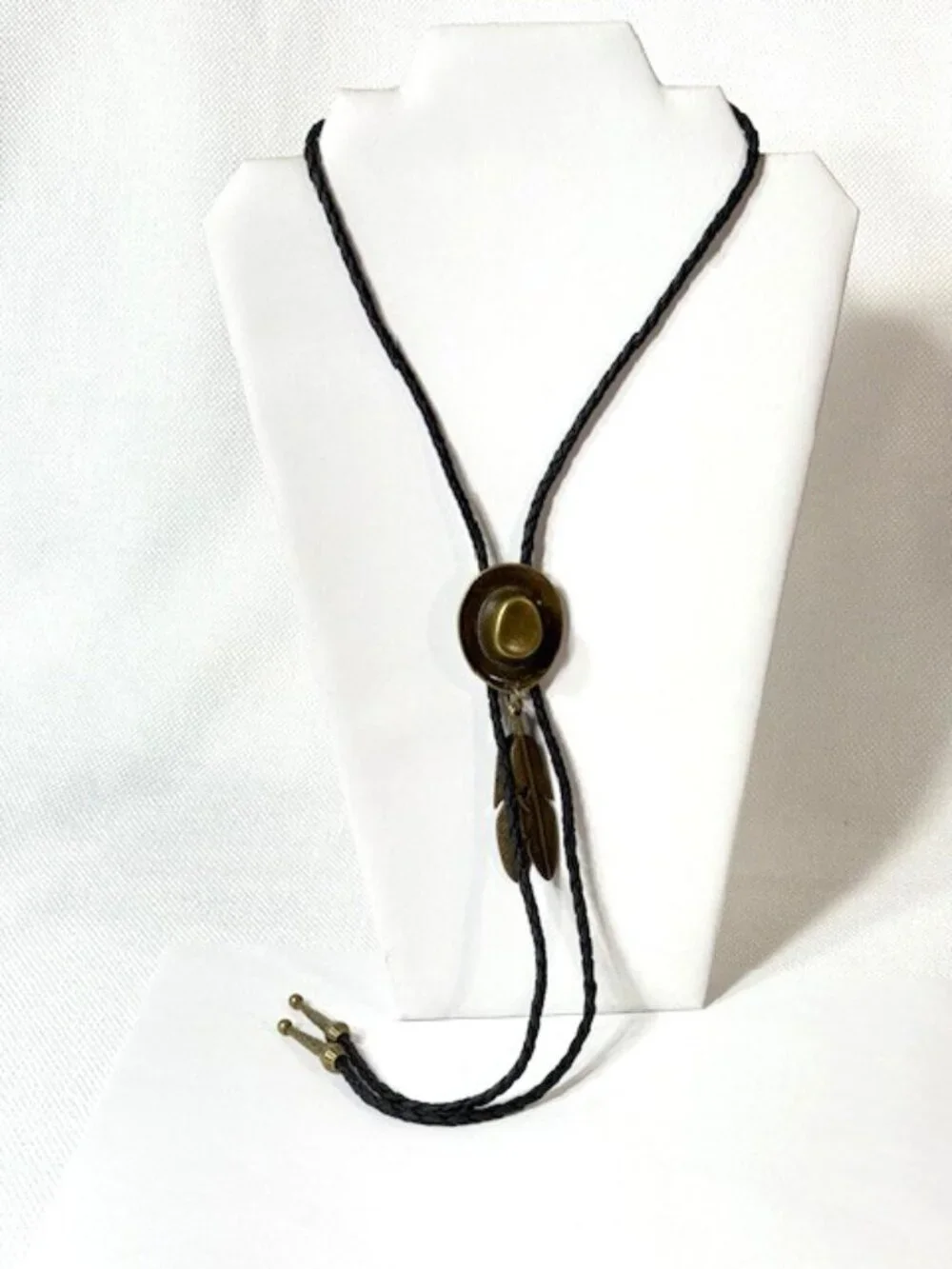 Gold-tone cowboy hat and feather, black cord western cowboy bolo tie.